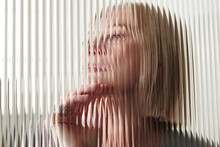 Horizontal Through Textured Glass Wall Portrait Of Pensive Senior Caucasian Woman With Blond Bob Cut Hair, Striped Distortion Effect