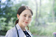 メインビジュアルにも！新緑背景で採用や転職で使えそうな逆光が美しいアジア系の見上げる女医さんのイメージ　アップ カメラ目線