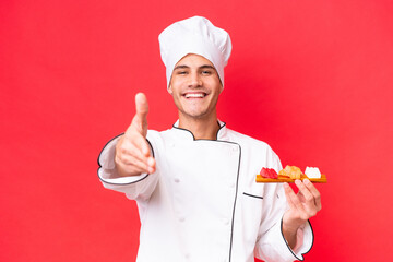 Wall Mural - Young caucasian chef man holding sashimi isolated on red background shaking hands for closing a good deal