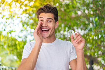 Wall Mural - Young caucasian man holding invisible braces at outdoors shouting with mouth wide open