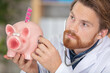 © auremar - doctor holding stethoscope to piggybank continaing blister of tablets