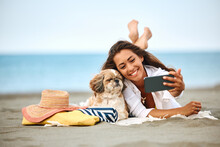 Happy Woman Taking Selfie With Her Dog During Summer Day On Beach.