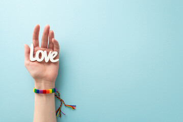 Sticker - A pastel blue background complements the first person top view image of a woman's hand donning a rainbow bracelet and holding the word 