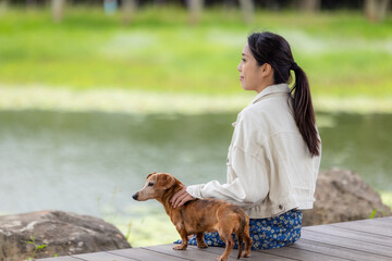 Wall Mural - Woman with her dachshund dog sit on the wooden floor beside the lake