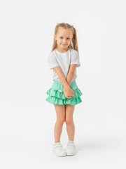 a caucasian girl with long hair 5 years old in a t-shirt and a green skirt stands with her arms and 