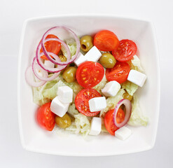 Wall Mural - mixed vegetable salad with tomatoes, onions and feta cheese in a white bowl on white background