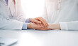© rogerphoto - Doctor and patient sitting near each other at the table in clinic office. The focus is on female physician's hands reassuring woman, only hands, close up. Medicine concept.