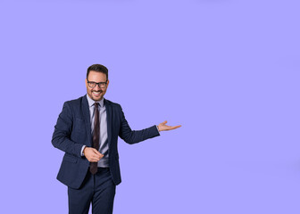 Portrait of smiling male professional executive showing copy space for business marketing. Young salesman dressed in elegant suit advertising something while standing isolated against blue background