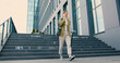 © serg - Young caucasian businesswoman came out of an office building, walking down the stairs and happy talking on the phone