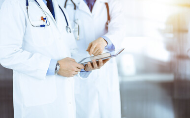 Wall Mural - Group of unknown doctors  use a computer tablet to check up some medical names records, while standing in a sunny hospital office. Physicians ready to examine and help patients. Medical help, insuranc