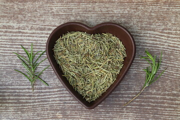 Dry organic background or texture of rosemary leaves. Healthy food concept . a wooden spoon with rosemary, a kind of green color and very fine sticks. leaning on a brown table.