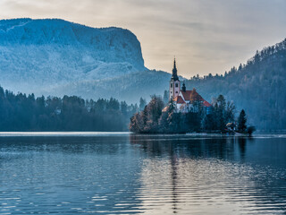 Wall Mural - Close up shot of the island Church in the middle of lake bled and snow the mountain during winter, Slovenia