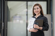 © Songsak C - Smiling young Asian businesswoman holding a digital tablet standing in an office.