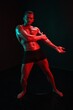 © SHOTPRIME STUDIO - Man bodybuilder posing muscles with nude fitness torso, isolated on black background in neon light. Advertising, sports, active lifestyle, colored light, competition, challenge concept.
