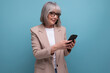 © Ivan Traimak - middle-aged woman in a stylish bow with a smartphone in her hands on a studio background with copy space