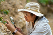 © Pornpimon - Female geologist using magnifying glass to examine and analyze rock, soil, sand in nature. Archaeologists explore the field. Environmental and ecology research.