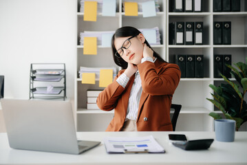 Overworked young Asian businesswoman office worker suffering from neck pain after had a long day at her office desk.