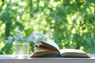 Jasmine flowers in vase and open book on table close up, abstract green natural background. symbol of spring season. beautiful romantic floral composition. reading, relax time, leisure concept.