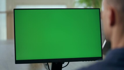 Over the Shoulder: Young Man Sitting at His Desk in Office Uses Desktop Computer with Green Mock-up Screen. Close up Green Screen Mock Up Display