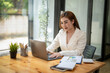 © Wasana - Happy Asian businesswoman sitting at her desk working on laptop computer. thinking work concept. typing a good work idea on her laptop.