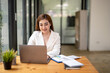 © Wasana - Happy Asian businesswoman sitting at her desk working on laptop computer. thinking work concept. typing a good work idea on her laptop.