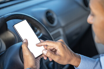 Detail of the hand of a driver holding a mobile phone with a blank screen on the steering wheel of the car with copy space.