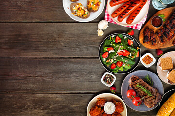 Summer BBQ food side border over a dark wood background. Variety of grilled meats, potatoes, vegetable dishes and smores. Overhead view with copy space.