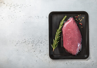 Wall Mural - Fresh raw beef fillet steak sealed in vacuum tray with pepper and rosemary on light kitchen table background.