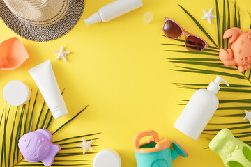 Child summer skincare idea. Top view flat lay of cosmetic bottles, sand molds for beach, sunhat, starfish, sunglasses and palm leaves on yellow background with empty area for text or advert