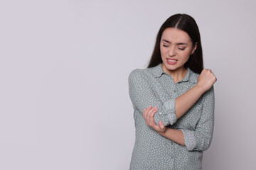 Canvas Print - Young woman suffering from pain in elbow on light grey background, space for text. Arthritis symptoms