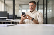 © Stock 4 You - Middle aged Hispanic business manager ceo using cell phone mobile app, laptop. Smiling Latin or Indian mature man businessman holding smartphone sit in office working online on gadget with copy space.