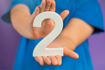 Fototapete - White number 2 in hand. The hand holding the number 2 symbolizes choice, partnership and duality, the choice between two alternatives, to combine the efforts of two people to achieve a common goal.
