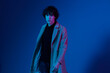 Man in fashion coat on dark blue background, neon light, style and trends, mixed light, men's fashion