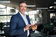 © insta_photos - Happy middle aged business man ceo wearing suit standing in office using digital tablet. Confident mature businessman professional company executive looking at camera holding tech device, portrait.
