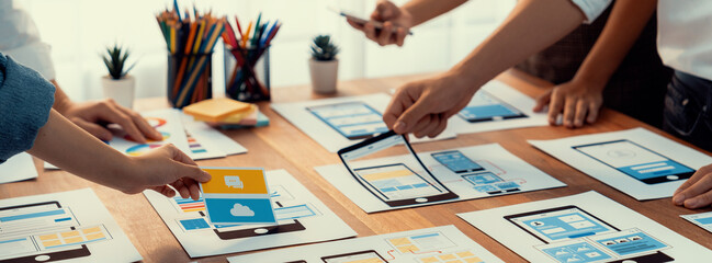 Panorama shot of front-end developer team brainstorming UI and UX designs for mobile app on paper wireframe interface. User interface development team planning for user-friendly UI design. Scrutinize