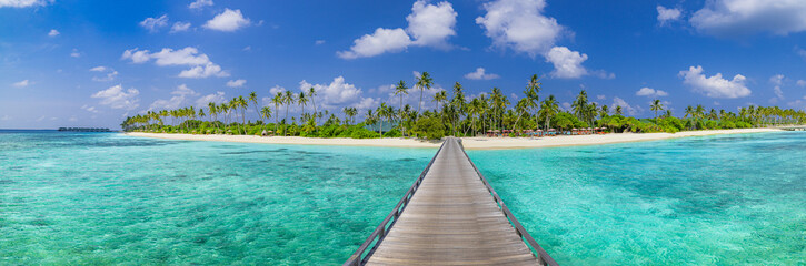 Luxury travel landscape. Water villas, wooden pier bridge leads to palm trees over white sandy shore close to blue sea, seascape. Summer panoramic vacation, beach resort on tropical island paradise