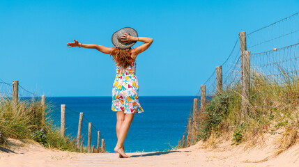 Wall Mural - Woman wearing dress with open arms standing in sand dune enjoying beautiful sea and beach view- Atlantic ocean in France