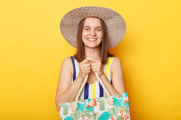 Optimistic smiling cheerful woman wearing swimsuit isolated on yellow background holding her beach bag being satisfied her resting near ocean.