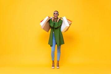 Full body studio shot portrait of fashionable African-American woman carrying shopping bags on yellow isolated background for summer sale concept