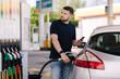 © Aleksandr - Bearded man refuelling car on gas station and looking into his smartphone. Man compares fuel prices