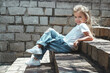 A little toddler girl sitting on the stairs and posing in jeans and white shirt. Future, success concept, kid fashion