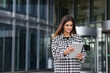 © kucherav - Young successful confident woman entrepreneur, CEO or an office worker stands with tablet near the business center, smiling