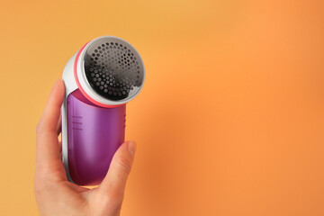 Poster - Woman holding modern fabric shaver on pale orange background, closeup. Space for text