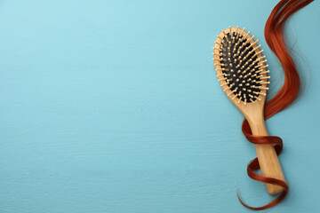 Brush and red hair strand on light blue wooden table, top view. Space for text