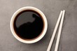 Bowl of soy sauce and chopsticks on grey table, flat lay
