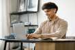© Prostock-studio - Middle Eastern Guy Using Laptop Websurfing Wearing Earbuds Sitting Indoor