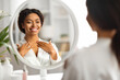 Black smiling woman looking in mirror and touching decollete zone
