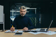 © Liubomir - Portrait of a senior man businessman accountant, financial director working in the office at a table behind a laptop and with documents. Confidently looks into the camera.