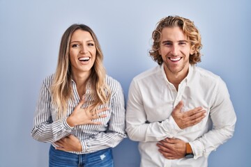 Canvas Print - Young couple standing over blue background smiling and laughing hard out loud because funny crazy joke with hands on body.