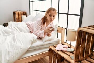 Sticker - Young caucasian woman drinking glass of water lying on bed at bedroom